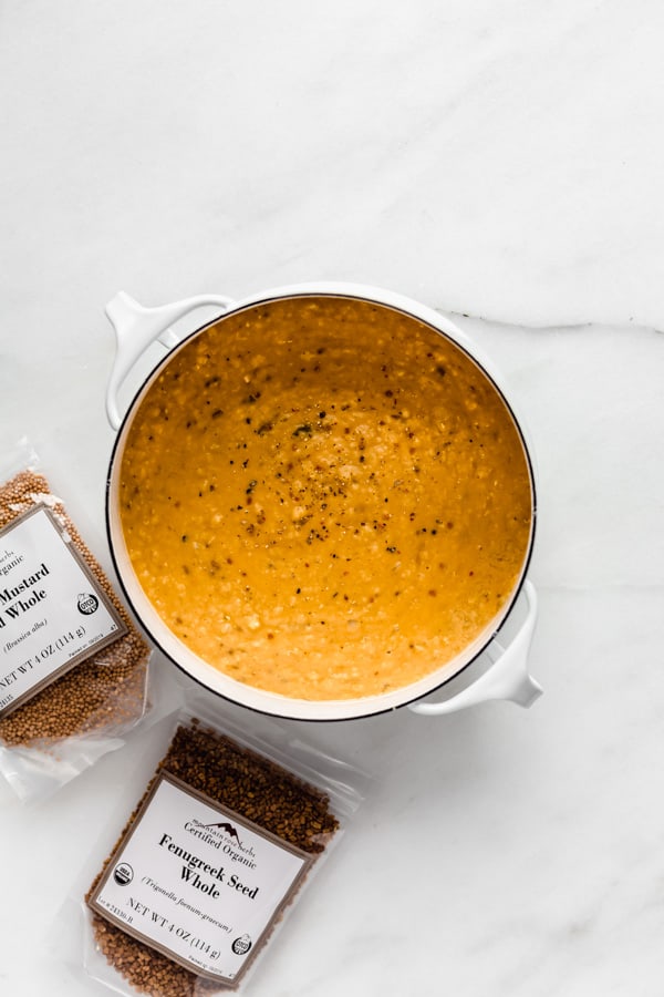 a pot of red lentil dal with herbs on the side