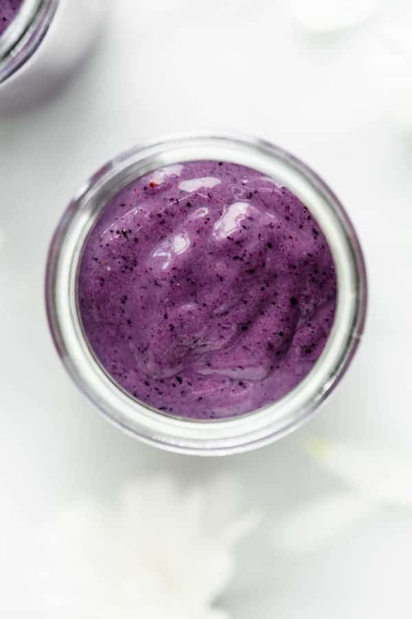 glass cup of healthy breakfast blueberry smoothie surrounded with white flowers 