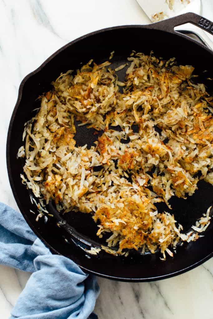 shredded hash browns being cooked in a cast iron skillet 