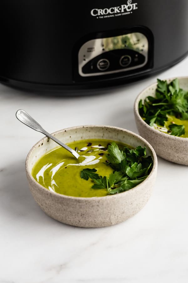 a bowl of broccoli soup with a crockpot in the back