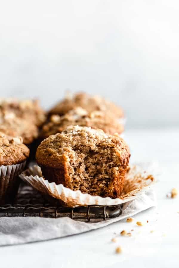 cooling rack filled with healthy breakfast banana nut muffins, with a bite taken out of one muffin on top of a grey linen