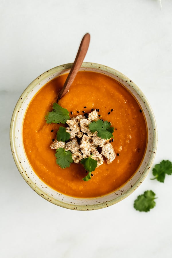 a bowl of orange soup with cilantro on the side