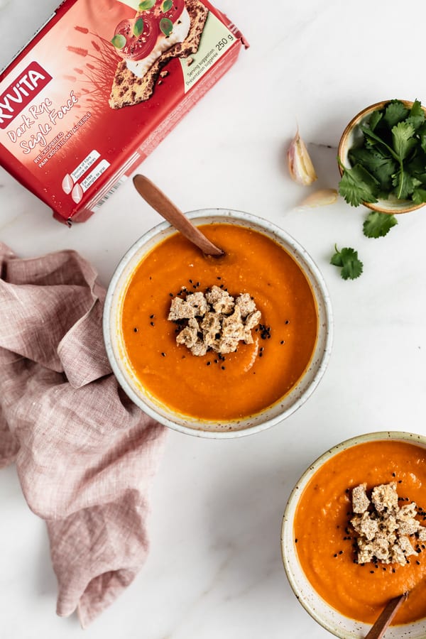 a bowl of sweet potato lentil soup on a marble board with a pink napkin, bowl of cilantro and box of Ryvita crisp breads on the side