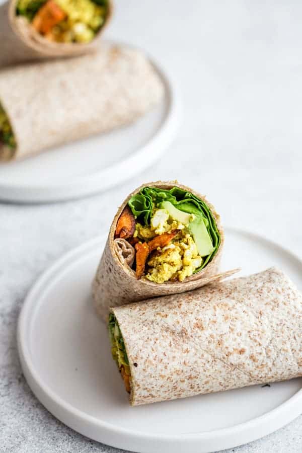 breakfast burrito cut in half on a white plate, with another breakfast burrito behind it