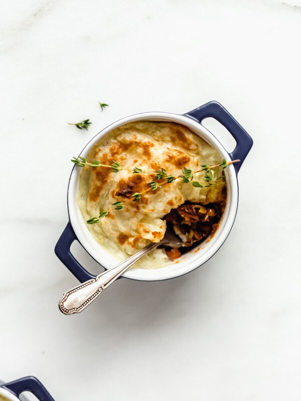 a vegan lentil shepherd's pie in a small blue ramekin with a spoon in it