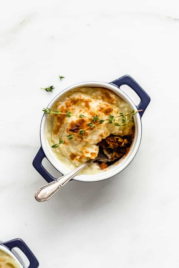 a vegan lentil shepherd's pie in a small blue ramekin with a spoon in it