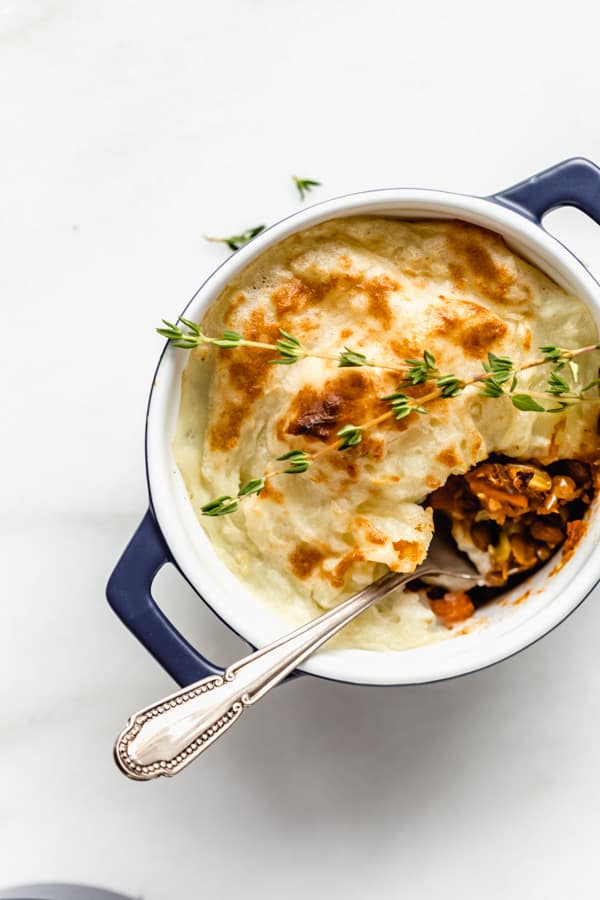 a spoon scooping a spoonful of lentils out of a mini vegan lentil shepherd's pie