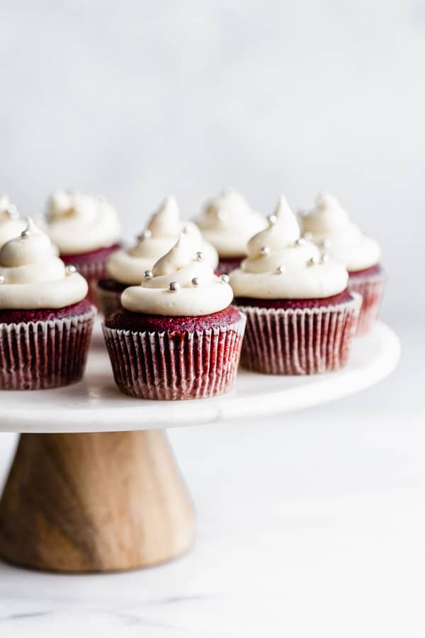 vegan red velvet cupcakes with cream cheese frosting and silver sprinkles on a marble and wood cakestand