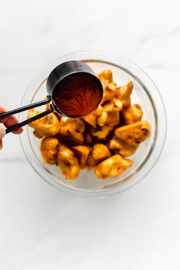 a measuring cup pouring buffalo sauce into a bowl of buffalo cauliflower wings
