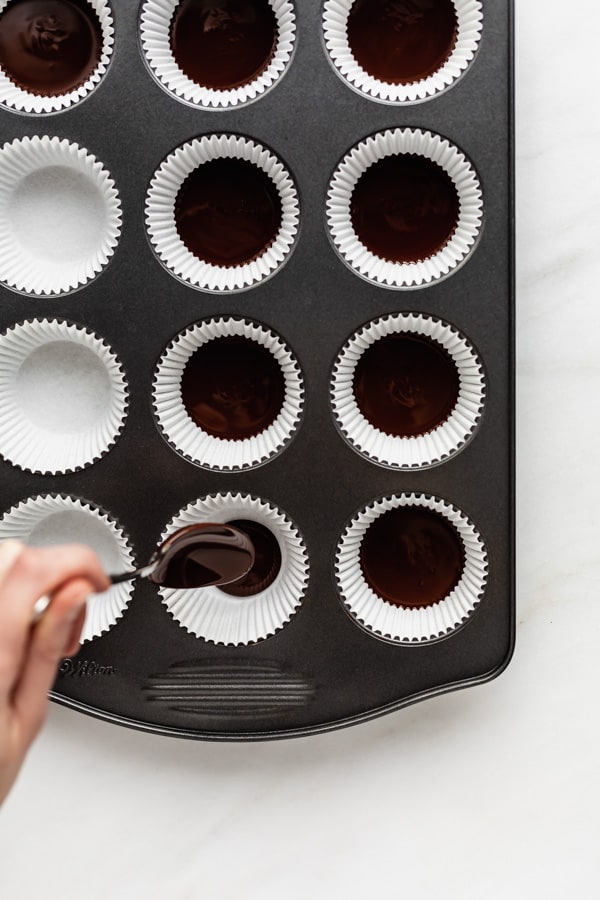 a hand spooning melted chocolate into a muffin pan with muffin liners