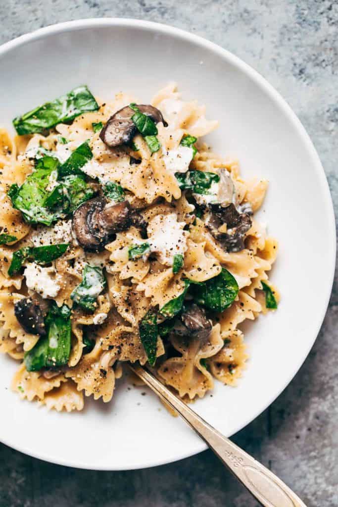bowtie pasta with mushrooms, spinach, and a cheesy cream sauce in a white bowl with a vintage silver spoon 