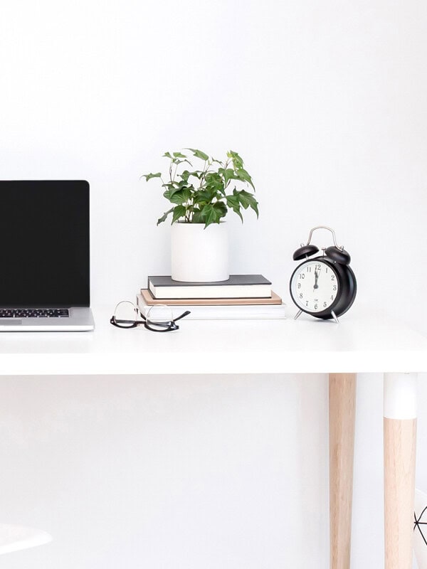 A clock, stack of books and plant on a white desk