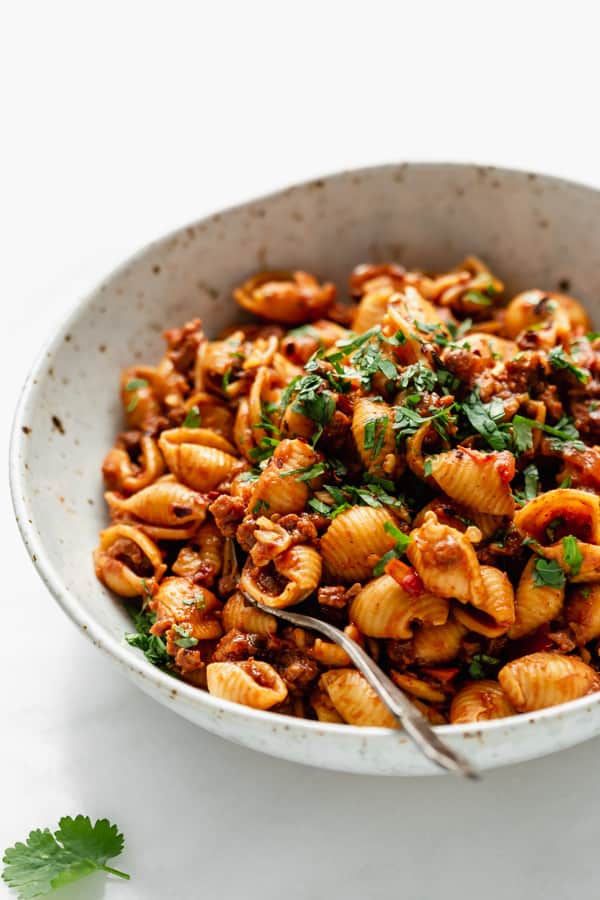A close up of shell noodles with taco pasta sauce in a white speckled bowl
