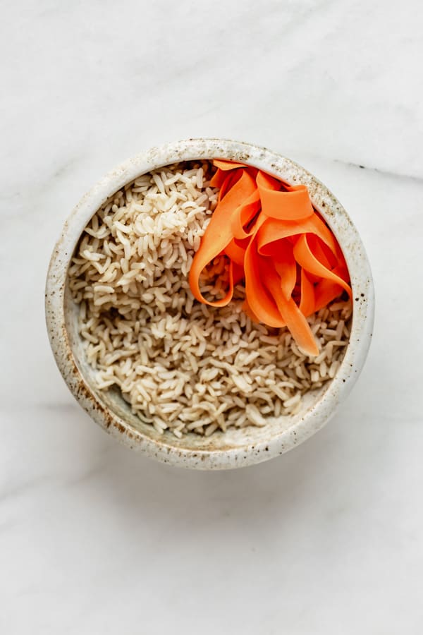 a ceramic bowl with brown rice and carrots in it