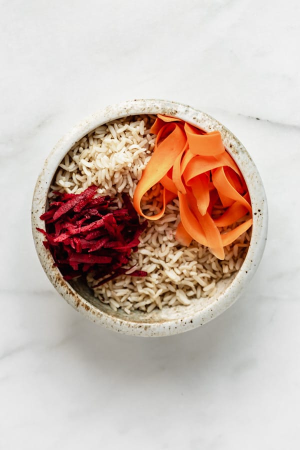 a white ceramic bowl with brown rice, shredded beets and carrots