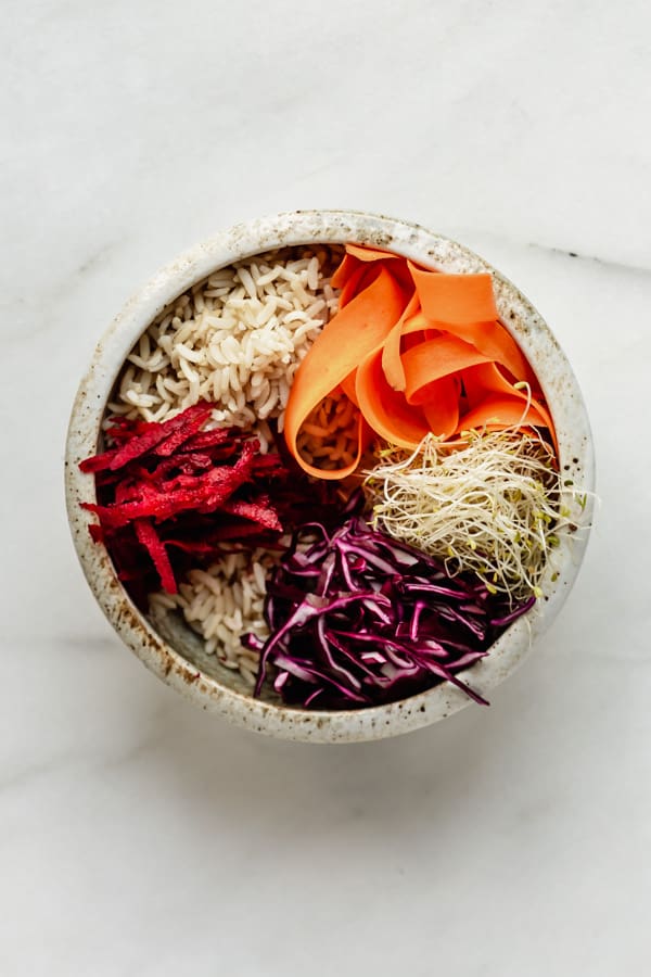 a white ceramic bowl with brown rice and veggies in it