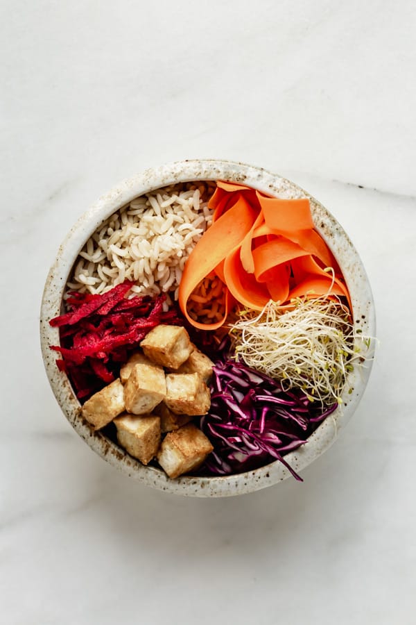 a white ceramic bowl with brown rice, tofu and veggies in it