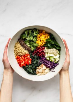 two hands holding a bowl of chopped vegetables and quinoa