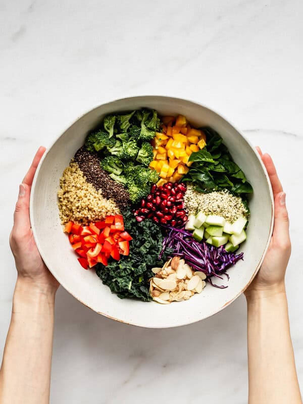 two hands holding a bowl of chopped vegetables and quinoa