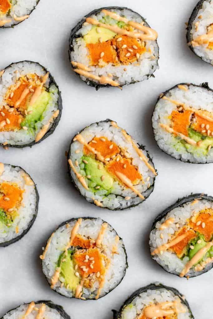 sweet potato tempura and avocado sliced sushi covered in toasted sesame seeds and sriracha mayo on a marble board