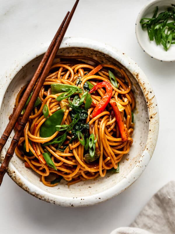 vegetable lo mein in a ceramic bowl with a side of sliced green onions
