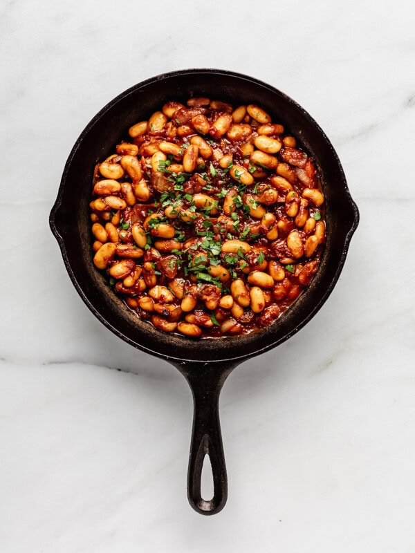 a cast iron skillet of maple baked beans on a marble counter
