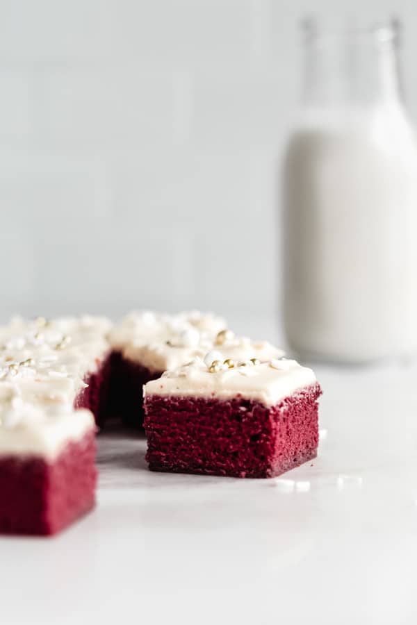 Red velvet brownies topped with icing and white and gold sprinkles on a marble board