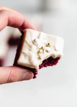 A hand holding a red velvet brownie with a bite taken out of it