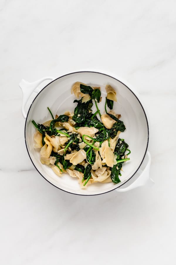 A white pot with spinach and artichoke hearts in it