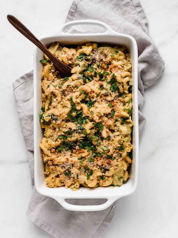 Vegan spinach and artichoke mac and cheese in a white baking dish with a serving spoon