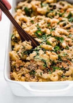 A serving spoon scooping up a spoonful of spinach and artichoke mac and cheese