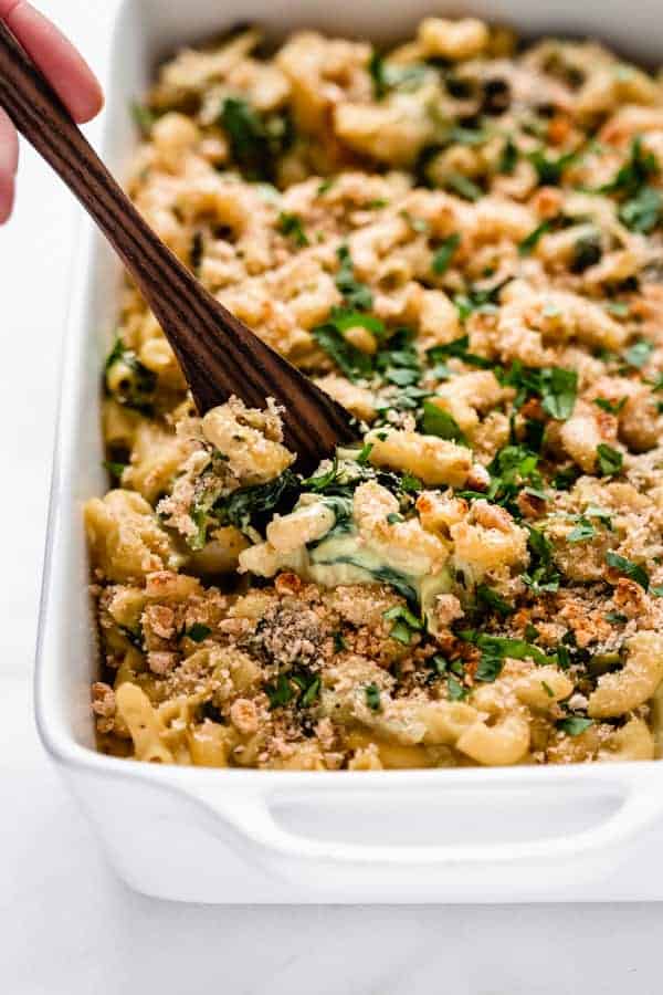 A serving spoon scooping up a spoonful of spinach and artichoke mac and cheese