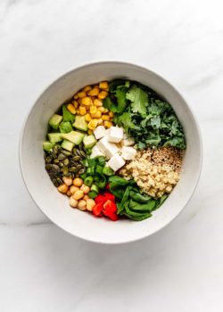 a bowl of quinoa salad with vegetables, feta cheese and seeds in it