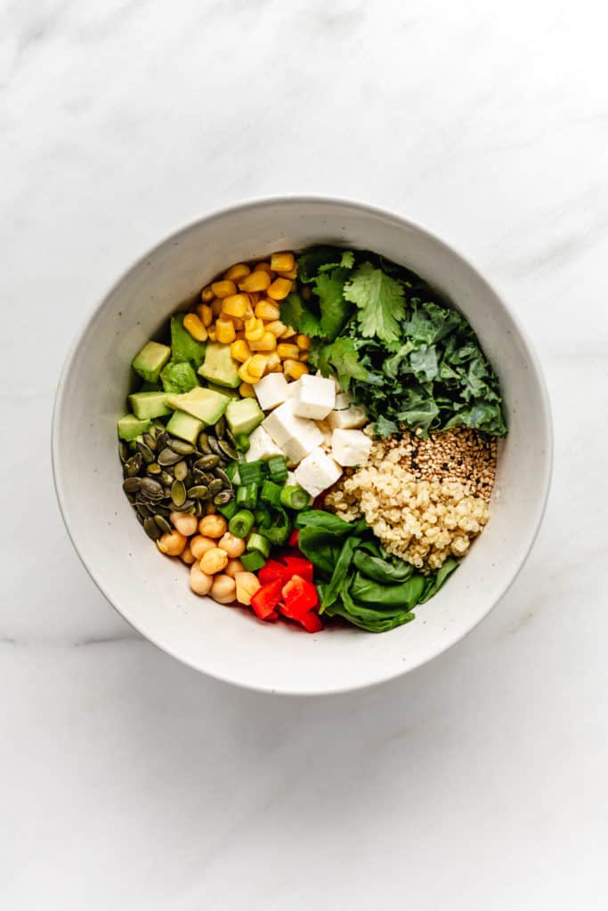a bowl of quinoa salad with vegetables, feta cheese and seeds in it