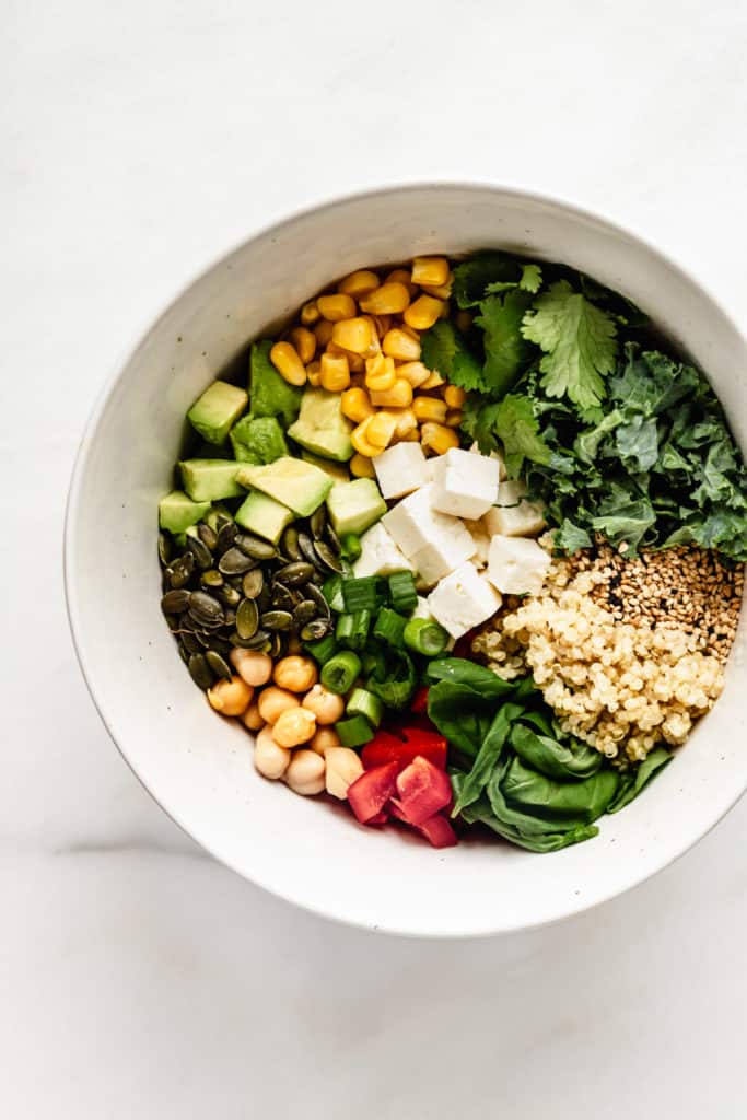 A salad bowl with vegetables, quinoa and feta cheese in it