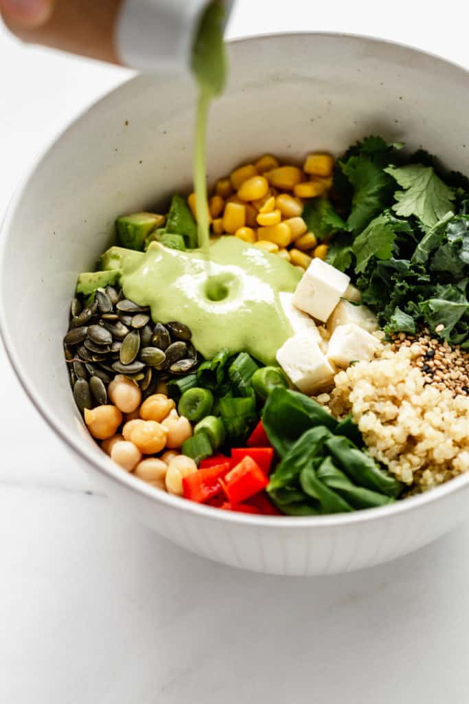 Green goddess dressing being poured into a bowl of vegetables