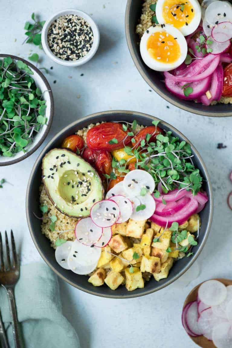 sliced radishes on top of a bowl with blistered cherry tomatoes, topped with black sesame seeds and microgreens and a half avocado