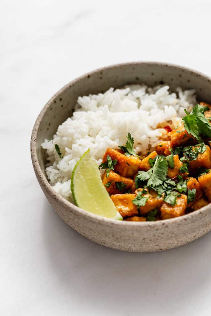 a bowl of coconut curry tofu with rice and a lime wedge