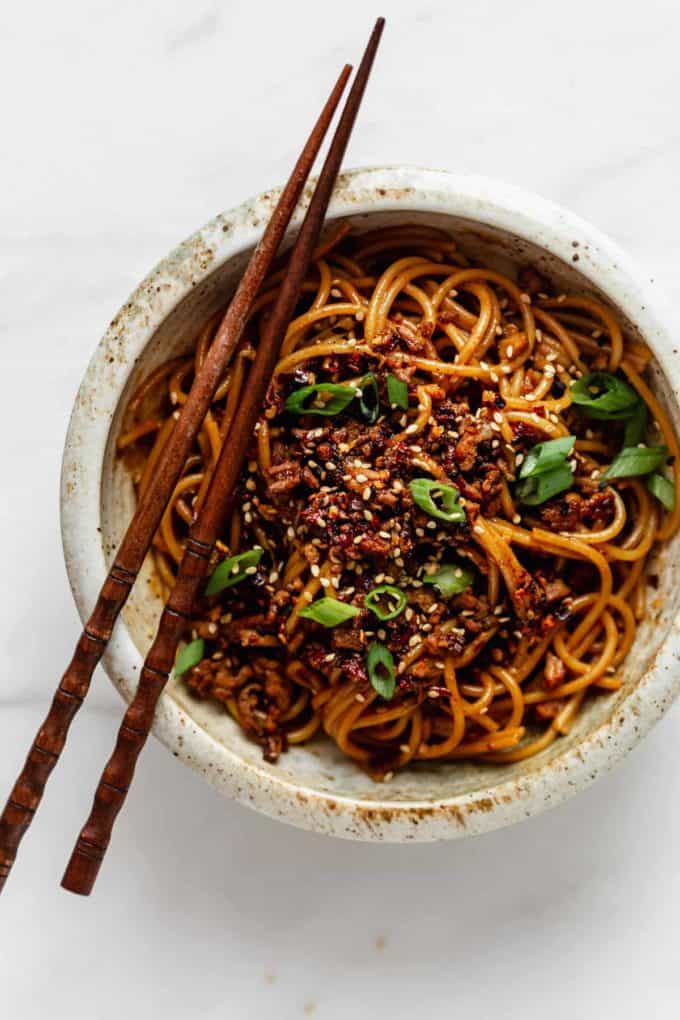 A bowl of vegan dan dan noodles with chopsticks on top