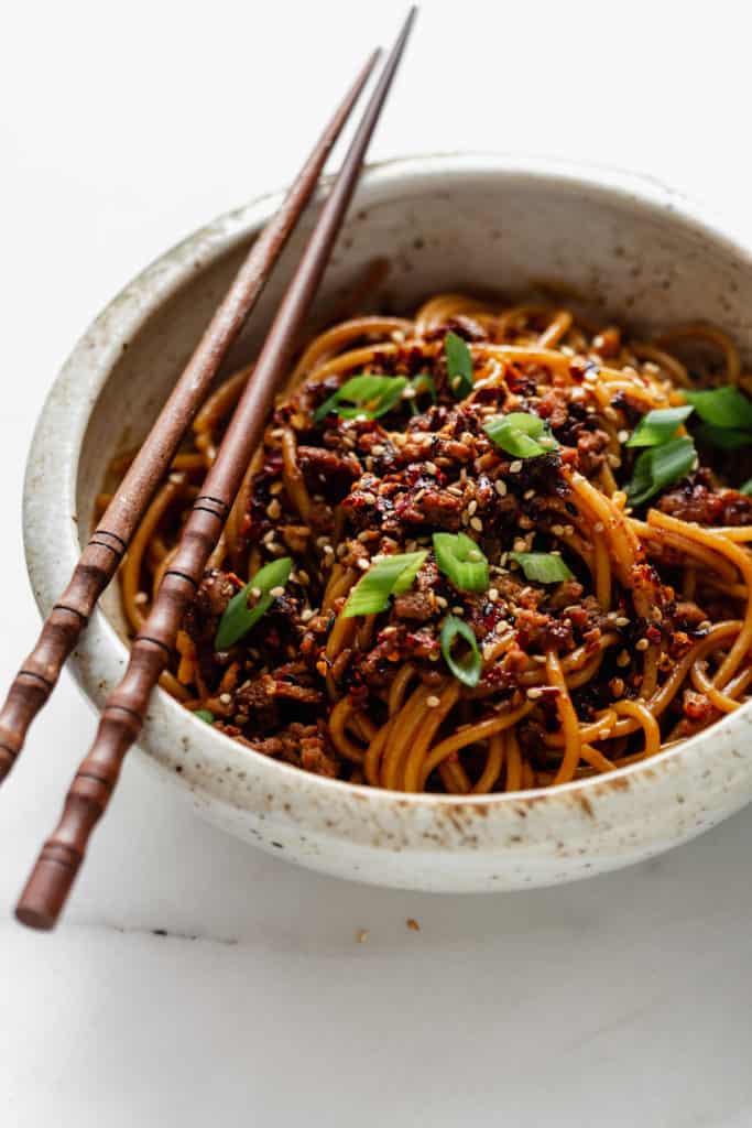 a bowl of vegan dan dan noodles with green onions on top
