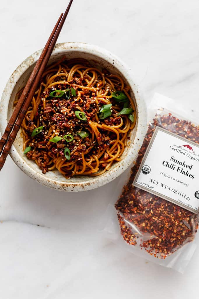 a bowl of dan dan noodles with smoked chili flakes on the side