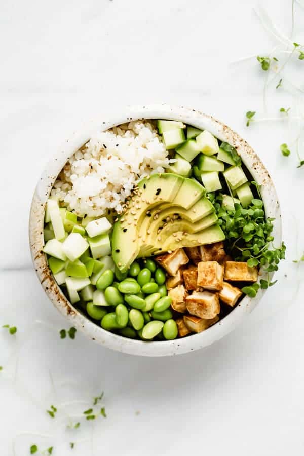 A vegan poke bowl with rice, tofu and veggies in it