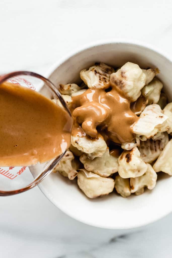 a measuring cup pouring peanut butter sauce onto baked cauliflower wings