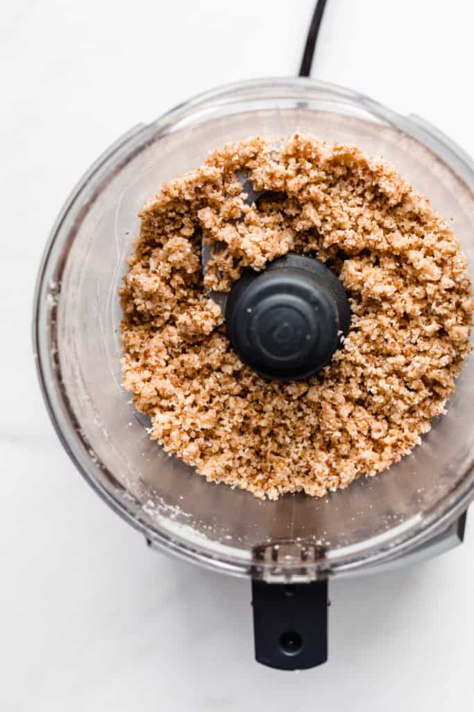 a food processor filled with crumbed almond flour, shredded coconut and dates