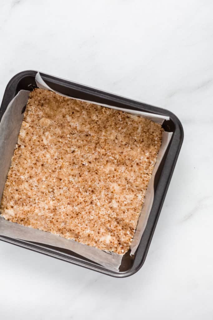 an 8x8 inch pan with raw almond flour cookie base in it