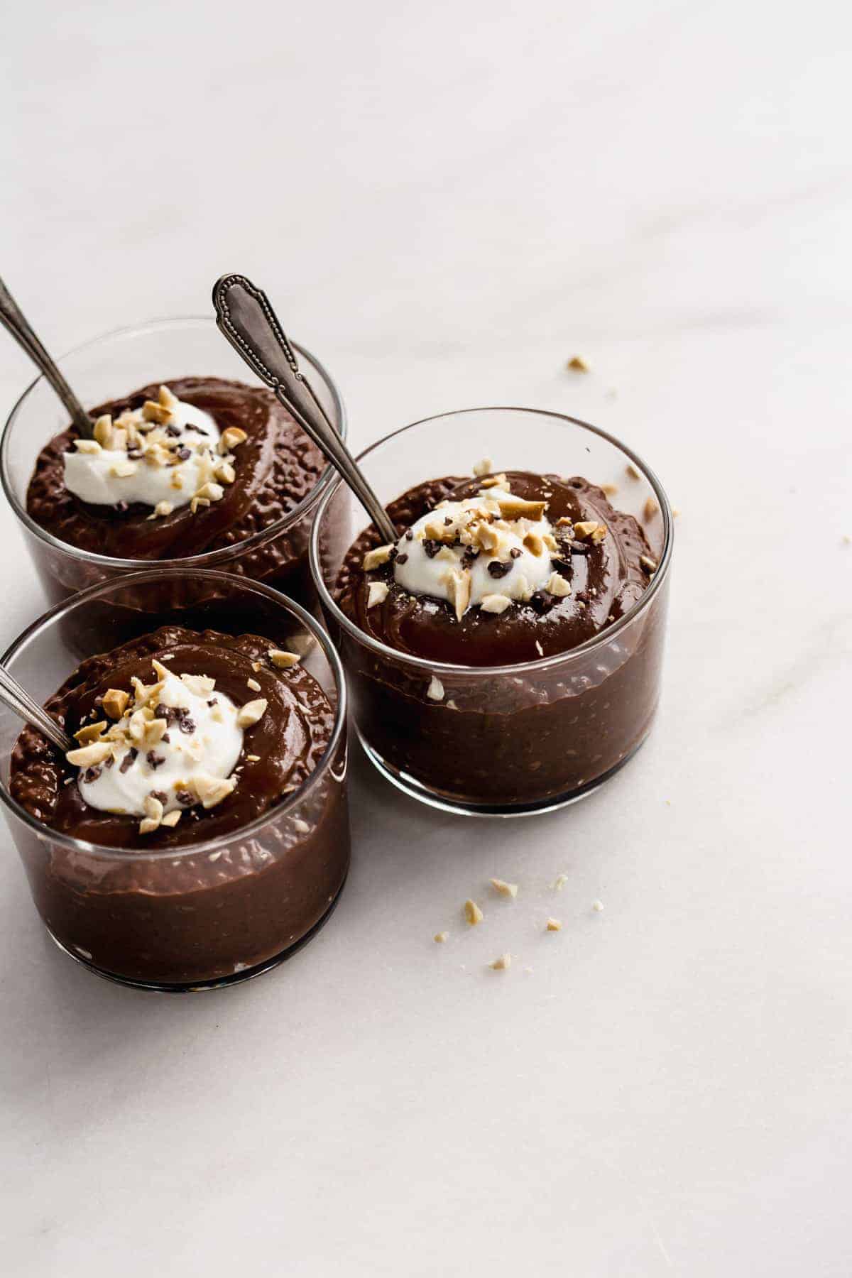 three cups of snickers chia pudding topped with yogurt, peanuts and cocoa nibs.