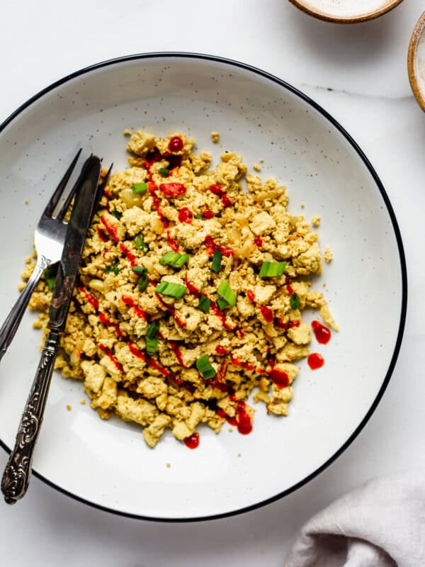 A bowl of scrambled tofu topped with chopped green onions and sriracha