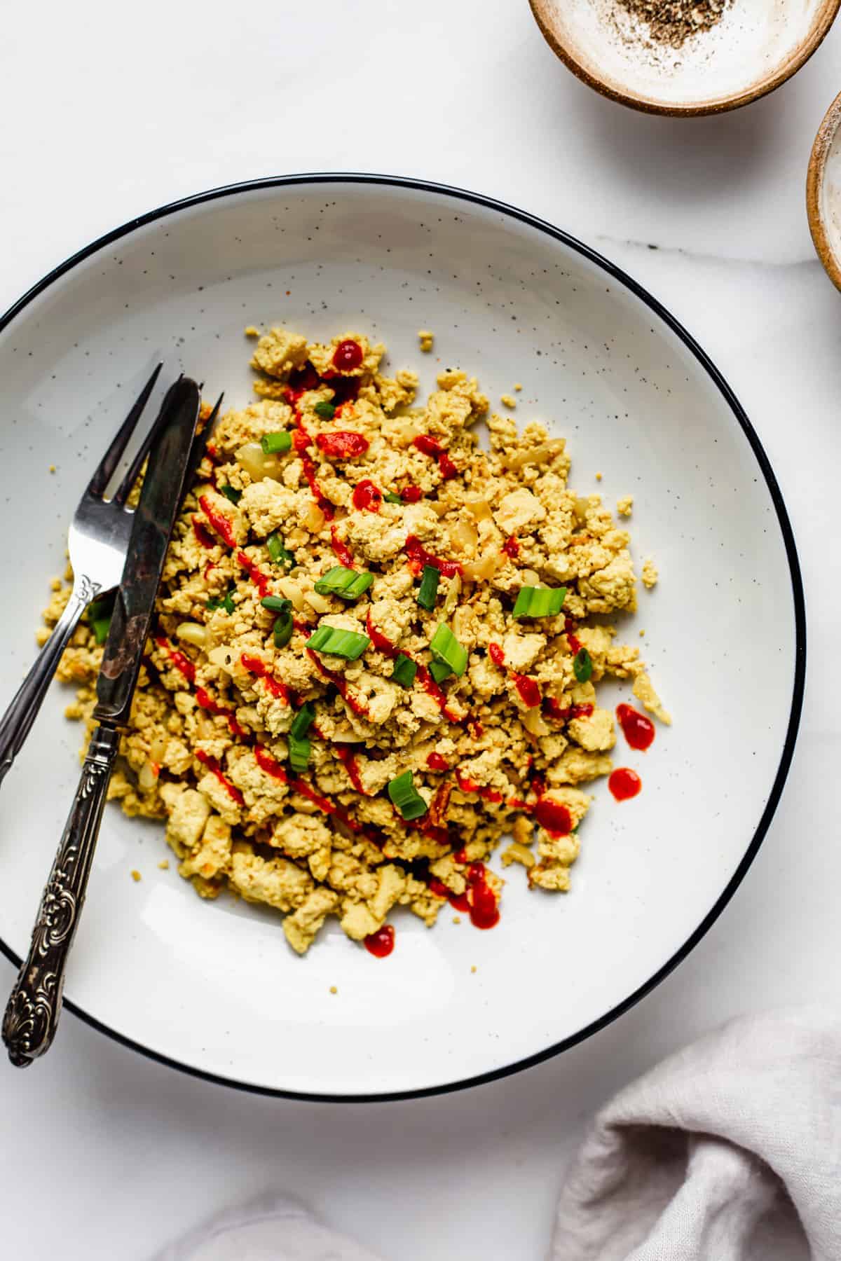 A bowl of scrambled tofu topped with chopped green onions and sriracha