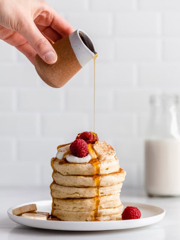 a hand pouring maple syrup onto a stack of vegan oatmeal pancakes