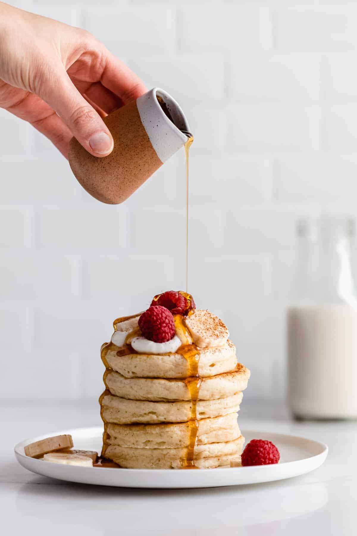 a hand pouring maple syrup onto a stack of vegan oatmeal pancakes